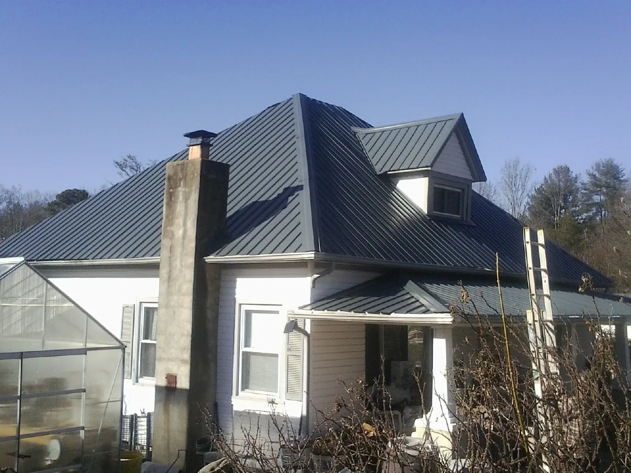 Dark blue standing seam metal roof on a white farmhouse with dormer — Slate & Tile Roof Repair by Roofing Brothers in May