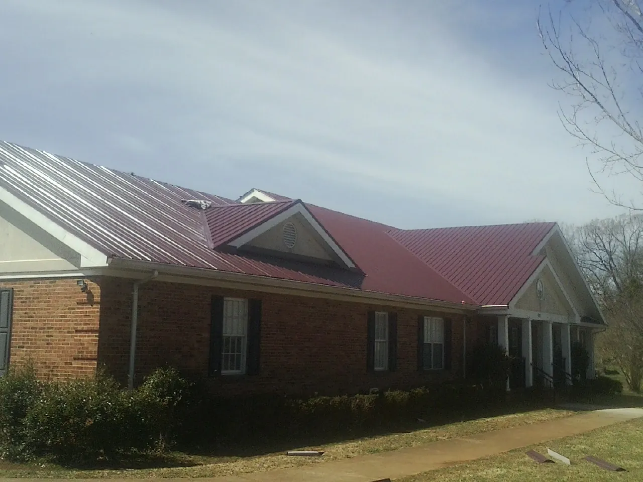 Red metal roof with gabled entries on a long brick building, from a Hail Damage Roof Repair job in May
