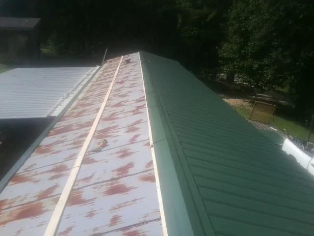 Old rusted panels beside newly installed green metal roofing — Wind Damage Roof Repair by Roofing Brothers in May