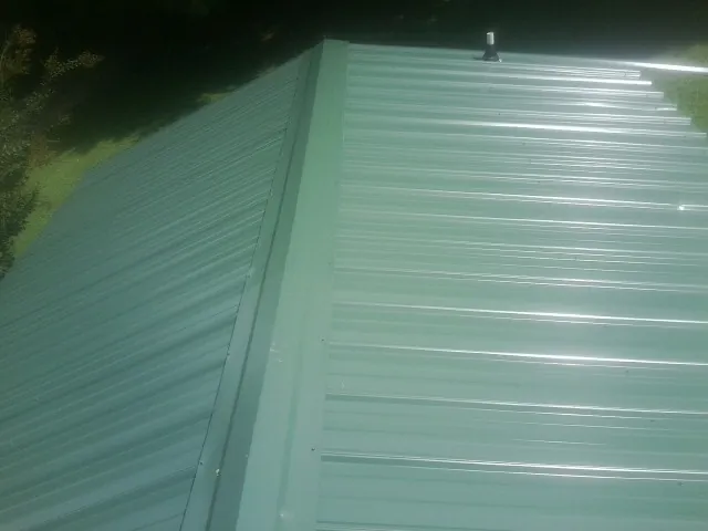 New green metal panels meeting at the ridge of a roof — Flat Roof Repair work by our crew in May