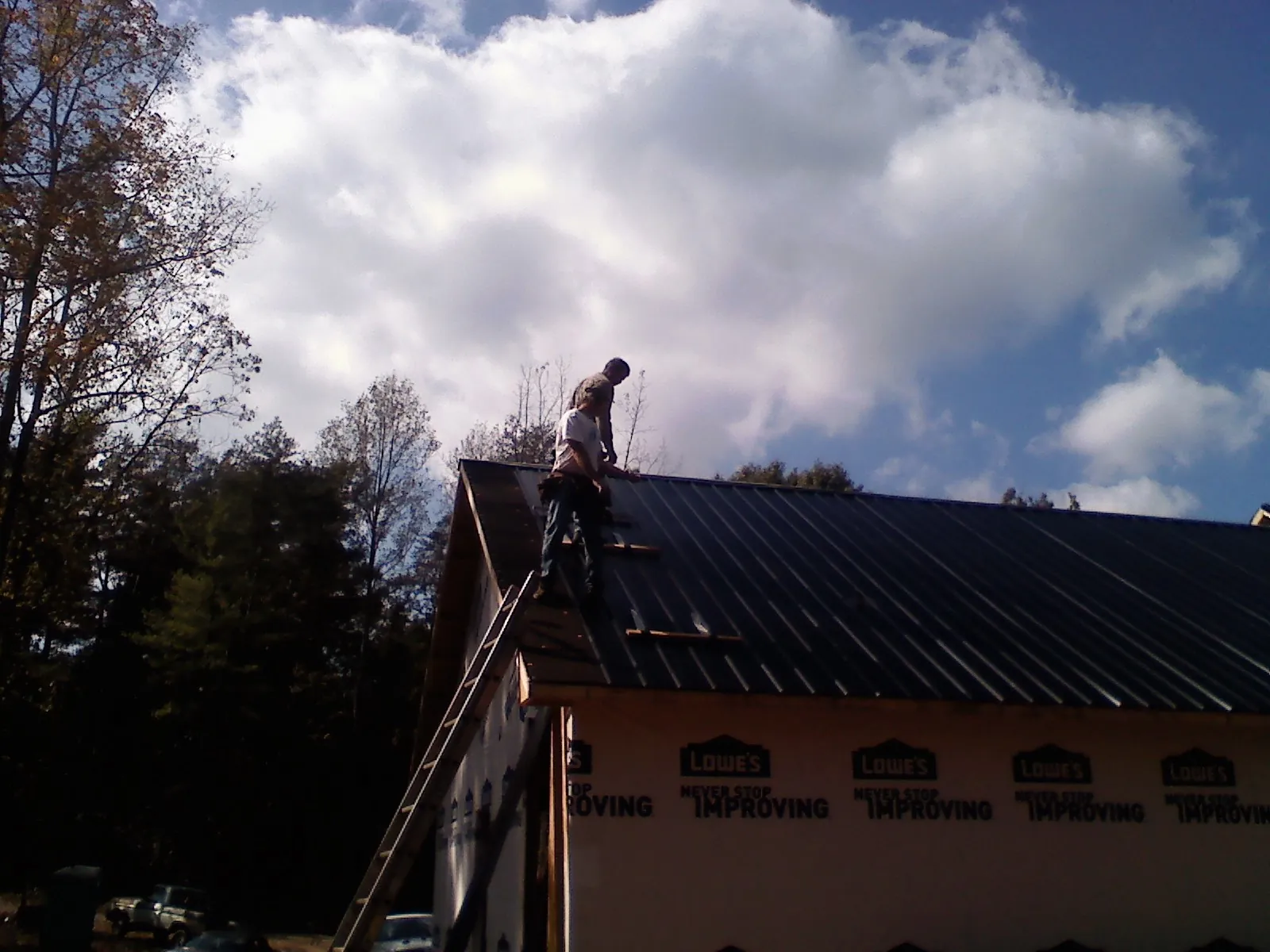 Roofer fastening dark metal panels high against a cloudy sky, from a Roof Inspection job in May